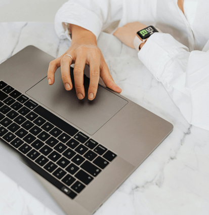 Person using a laptop on a marble table, wearing a smartwatch.